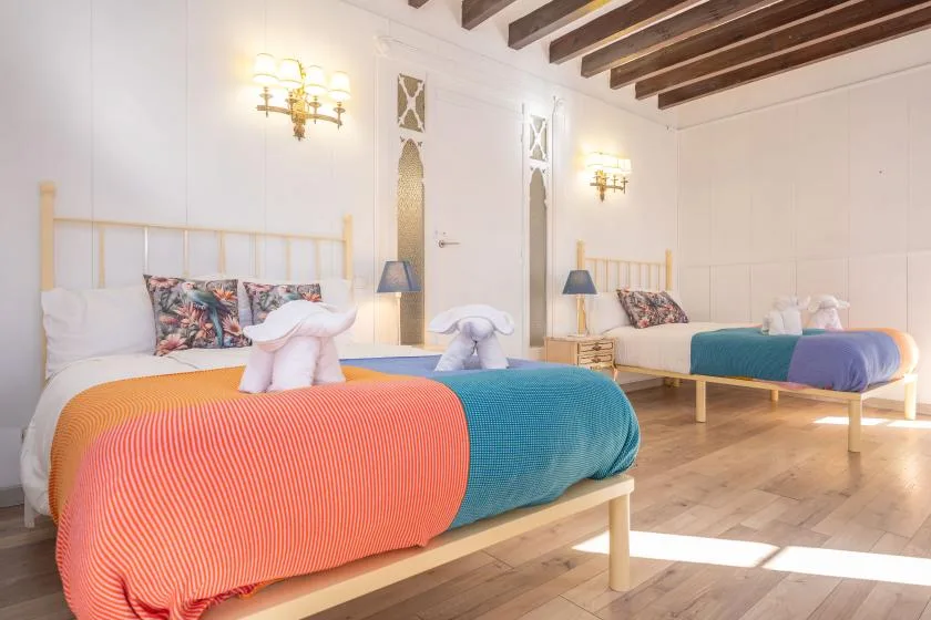 A bedroom with two beds, colorful bedding, and exposed wooden ceiling beams.