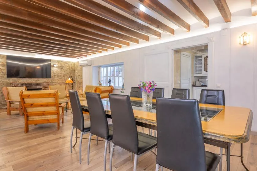 A dining area with a long table and chairs beneath exposed ceiling beams.