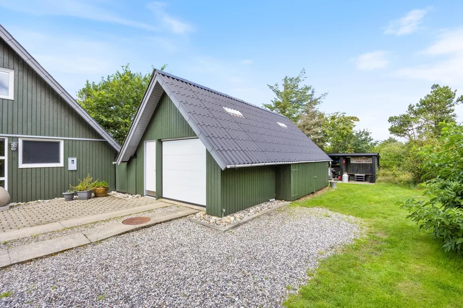A green outbuilding beside a gravel drive and grassy yard.