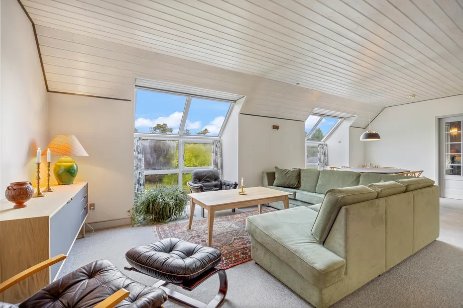 A bright living room with sloped ceilings, large windows, and seating around a coffee table.