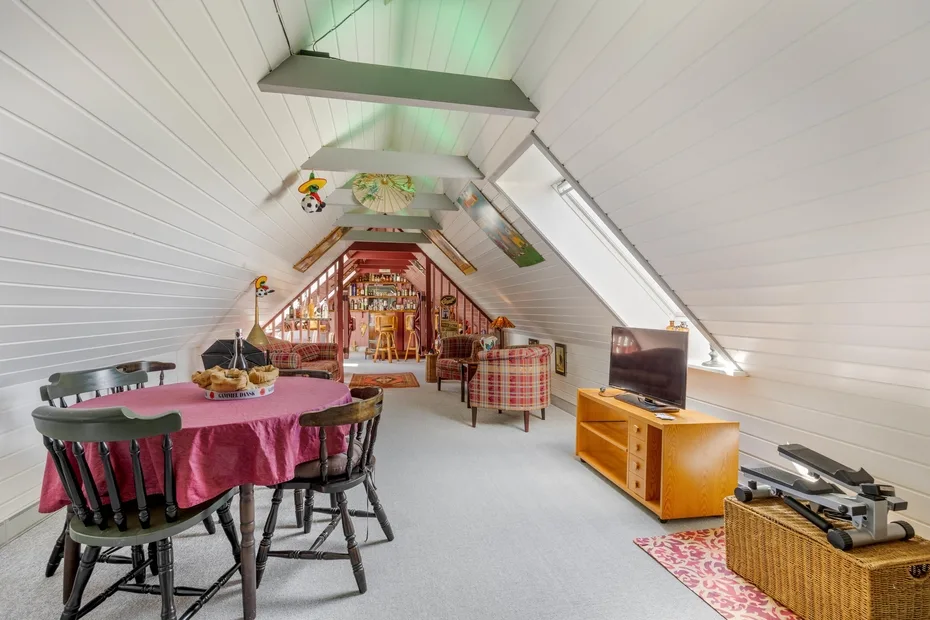A dining and living area beneath a sloped white ceiling, with a table and seating.