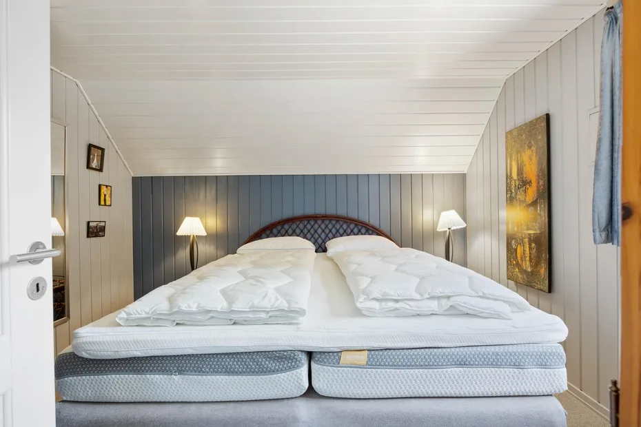 A bedroom with a large bed dressed in white bedding and bedside lamps.