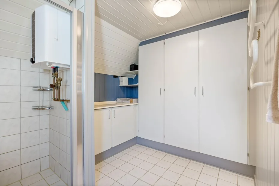 A tiled bathroom with white cabinets and a wall-mounted water heater.