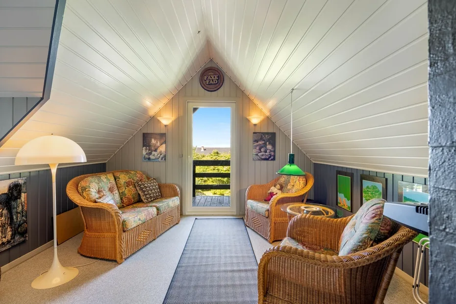 An attic sitting room with wicker seating around a central rug.
