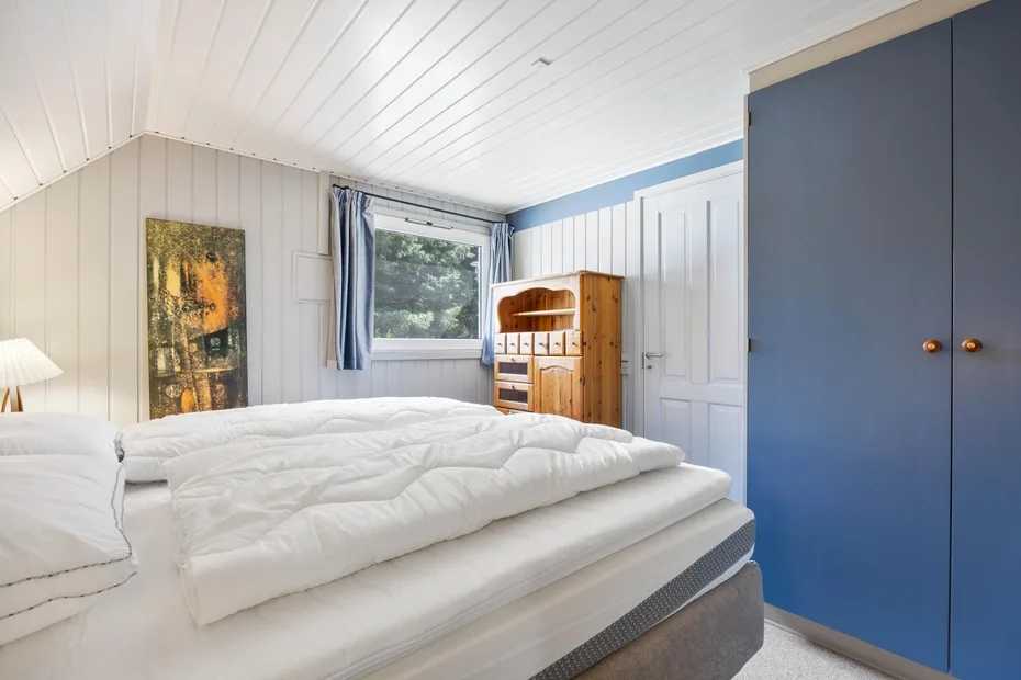 A bedroom with a bed, window, and wooden cabinet.