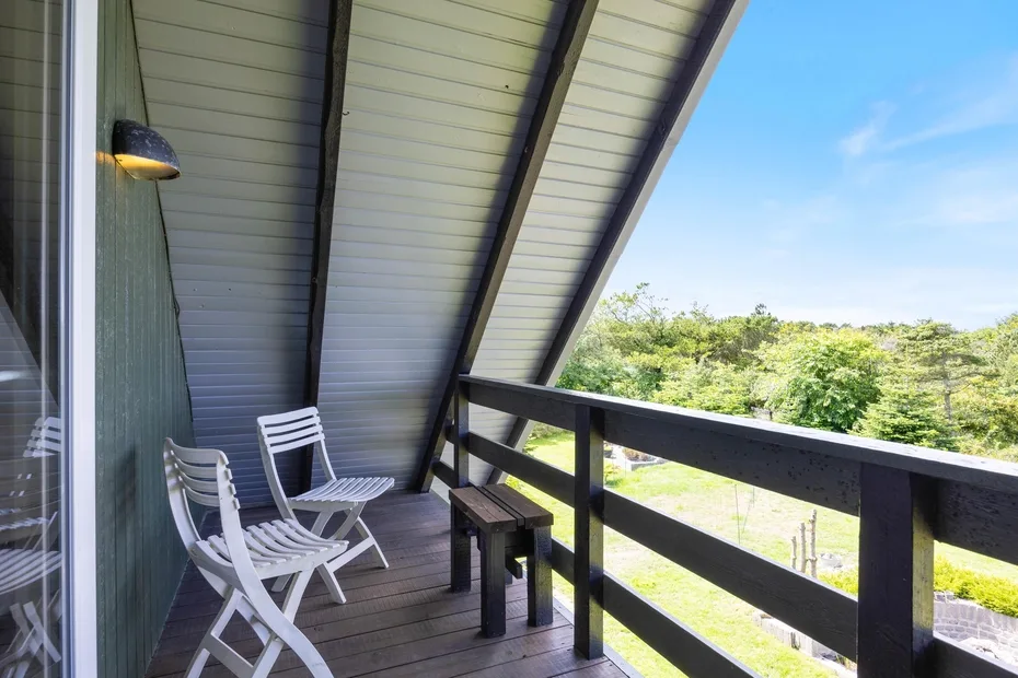 A covered balcony with seating overlooks green trees and open sky.