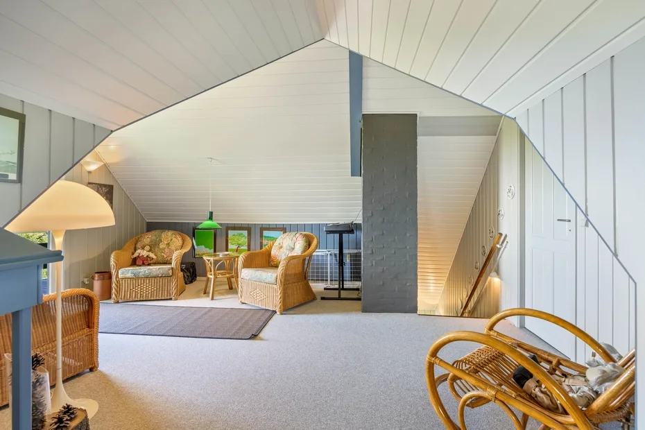 A bright attic sitting area with wicker seating and sloped white walls.