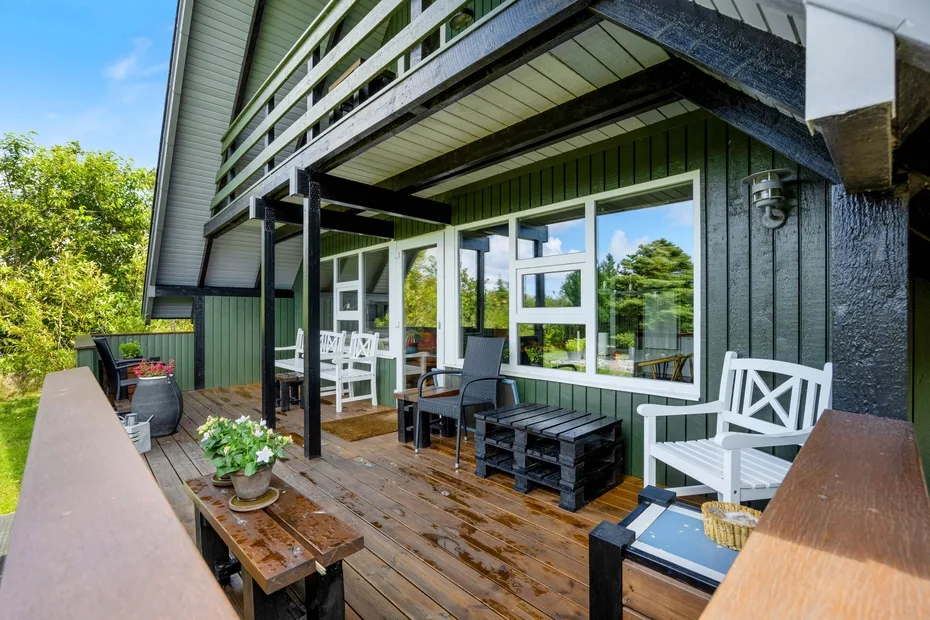 An outdoor deck with seating beside a house, overlooking green trees.
