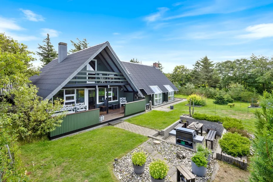 A modern house with a steep roof overlooks a garden patio and green lawn.