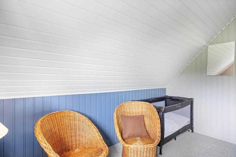 A bedroom with wicker seating and a dark-framed crib beneath a sloped ceiling.