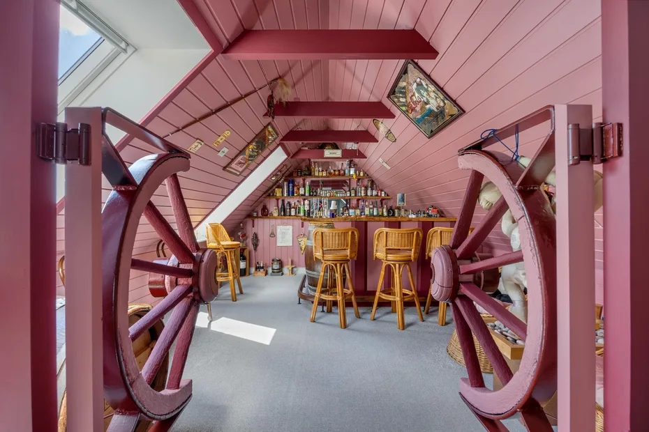 A pink attic bar with a counter and stools beneath sloped walls.