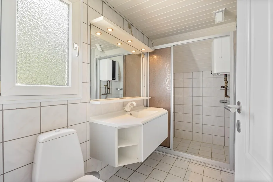 A tiled bathroom with a sink, mirror, toilet, and shower.