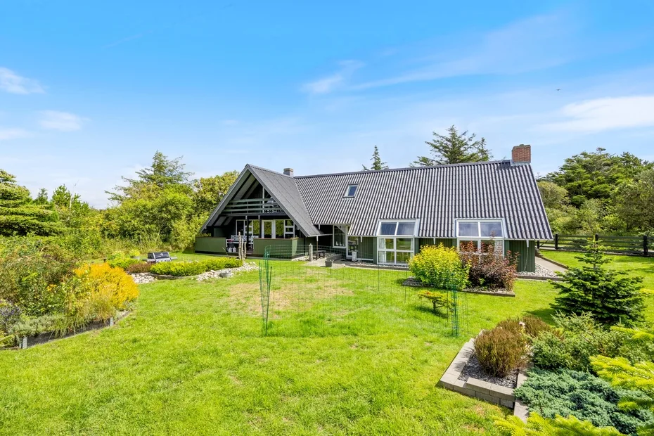 A house with a steep roof sits beside a spacious green lawn.