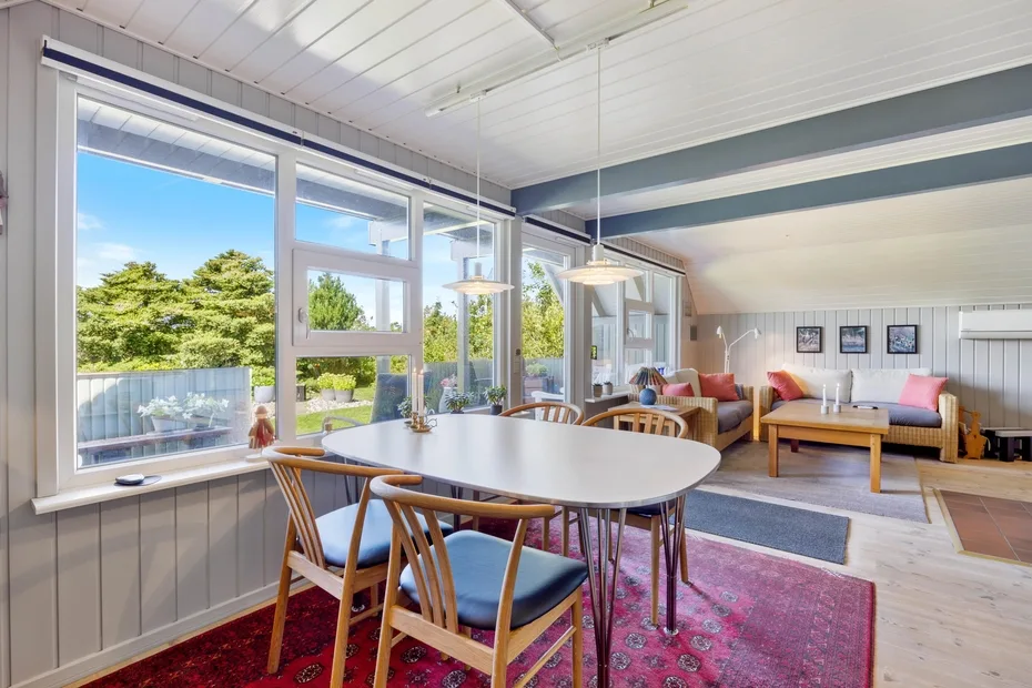 A bright dining and sitting area has large windows overlooking greenery.