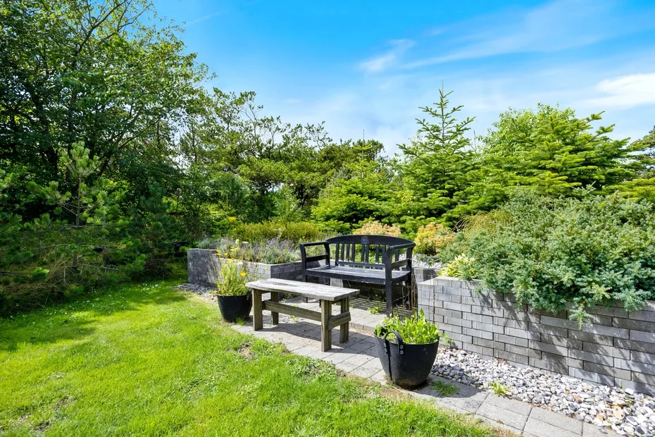 A garden patio with outdoor seating, surrounded by green trees and plants.