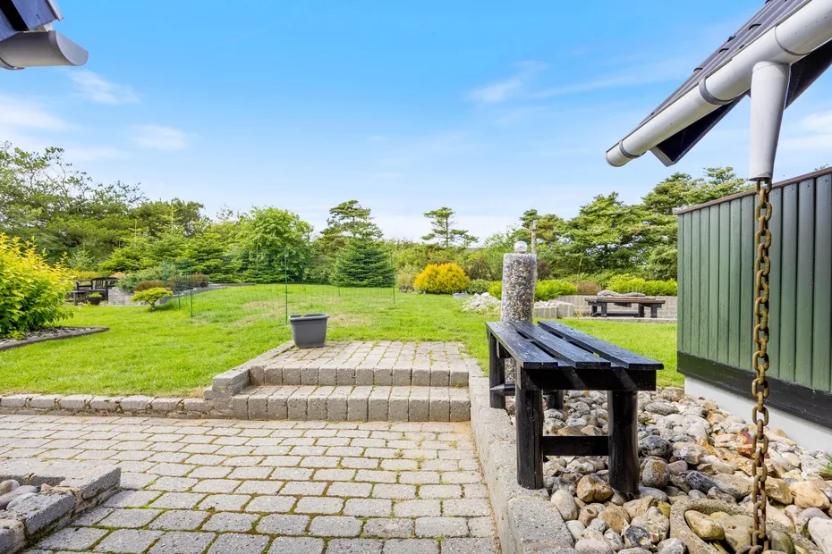 A paved patio opens onto a grassy garden with shrubs and outdoor seating.