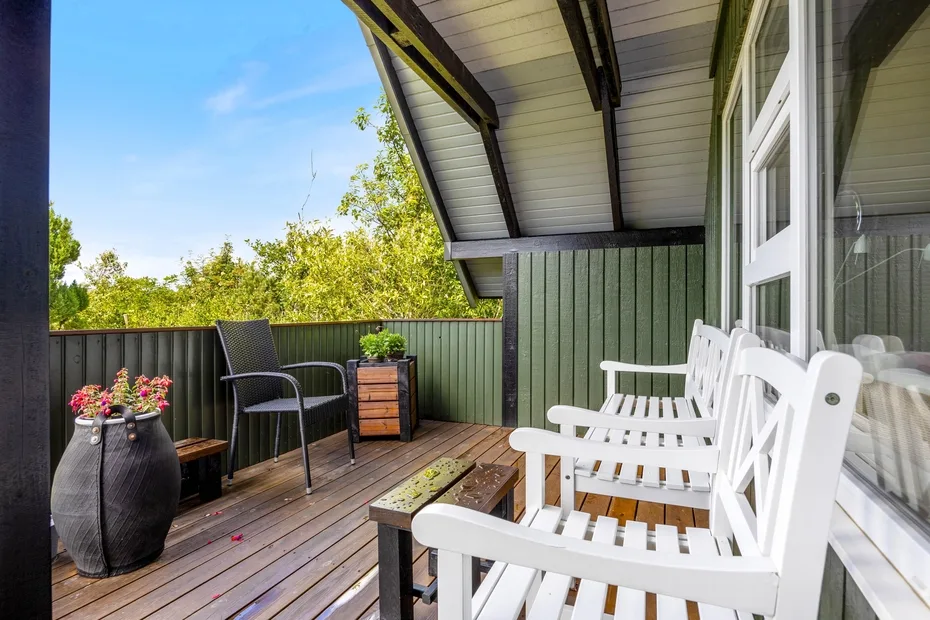 A covered outdoor deck with white seating and potted flowers.