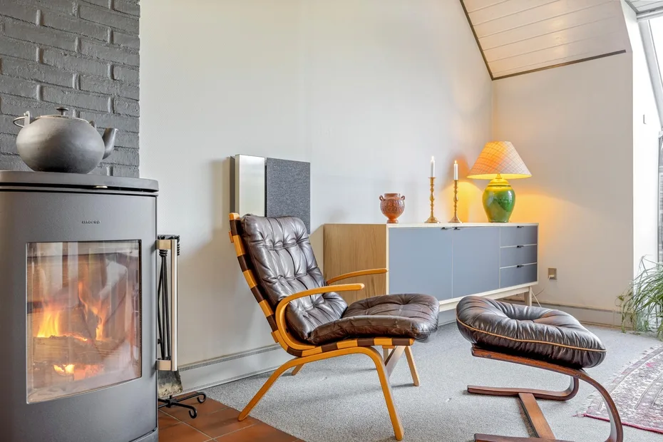 A living room with a lounge chair, matching footstool, and lit fireplace.