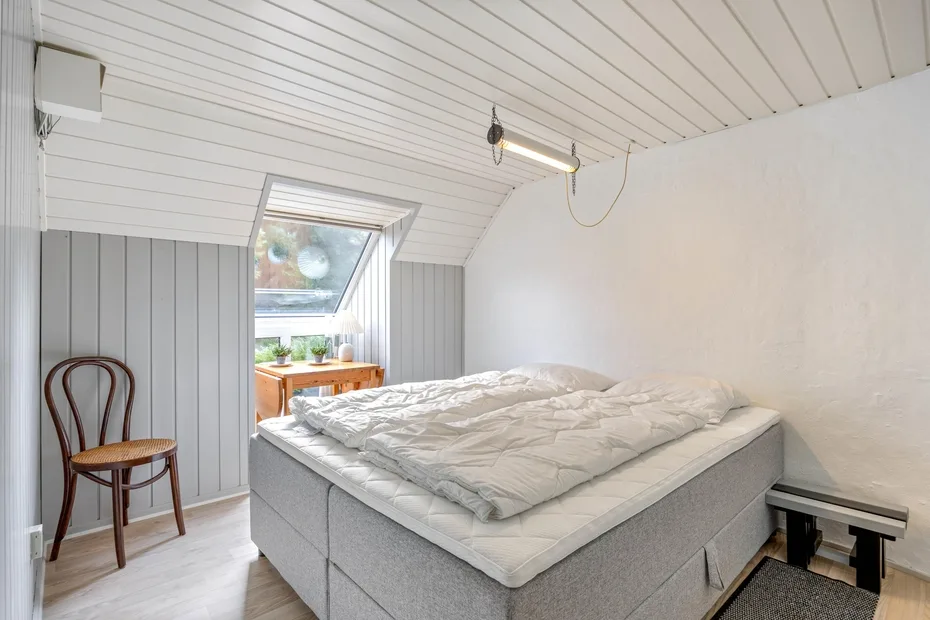 A compact bedroom with a bed beneath a sloped ceiling and a skylight.
