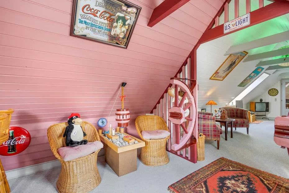 A pink attic sitting area has wicker seating beside a staircase and a patterned rug.