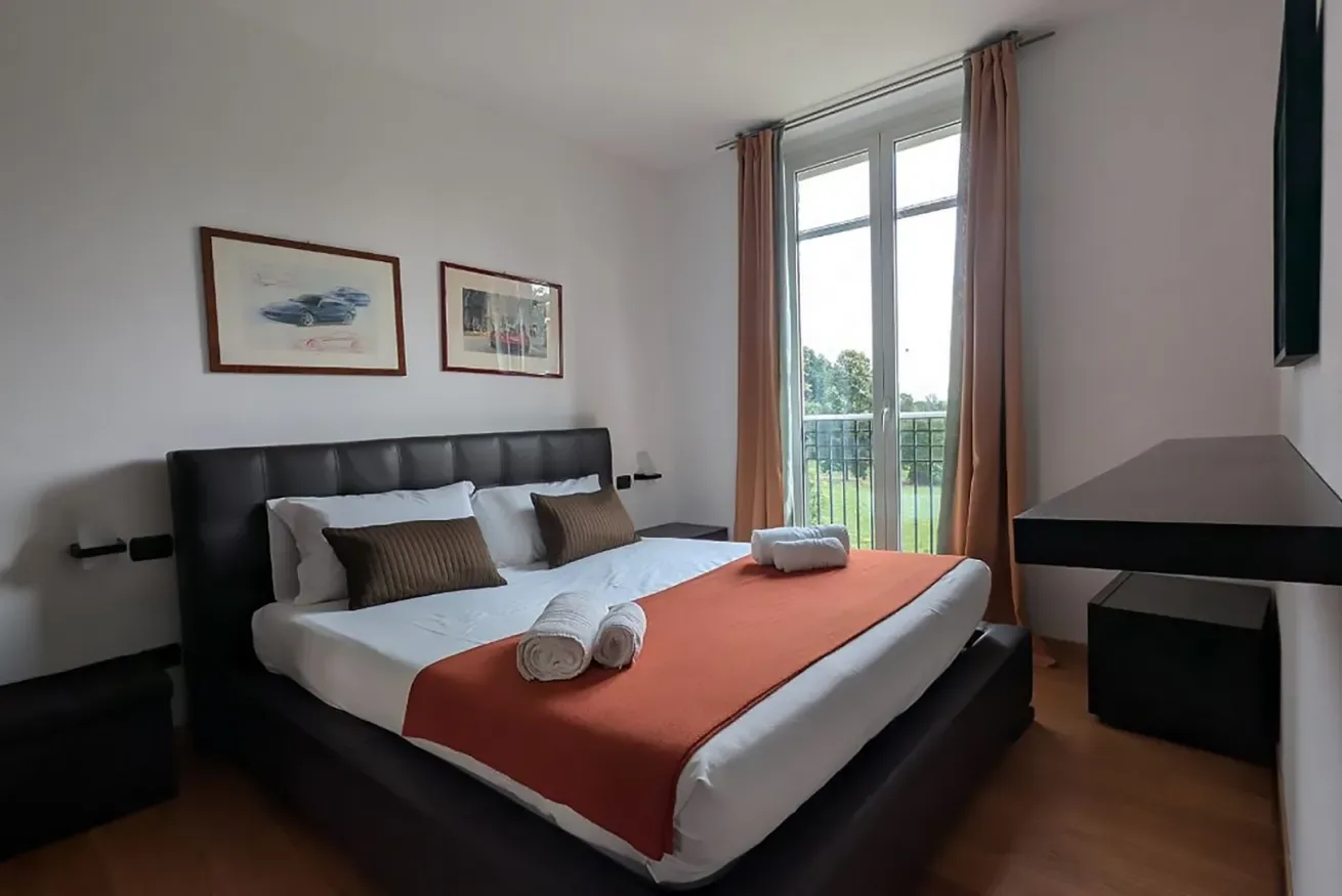 Un dormitorio con una cama bien arreglada junto a una puerta alta de vidrio.