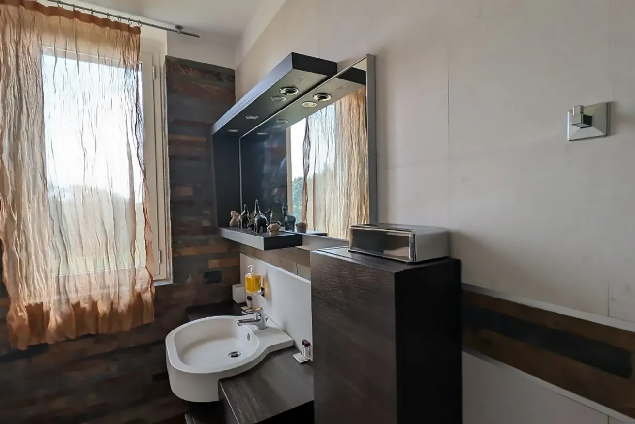 Un lavabo de baño con espejo y una ventana con cortinas transparentes.
