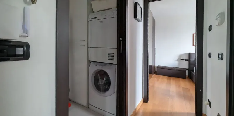 Un pasillo con una lavadora y vistas a un dormitorio.