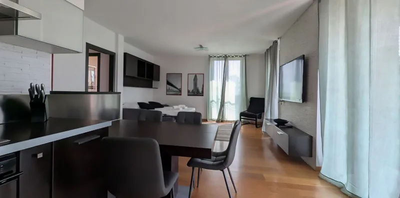 Una sala de estar y comedor modernos con mesa, asientos y grandes ventanales.