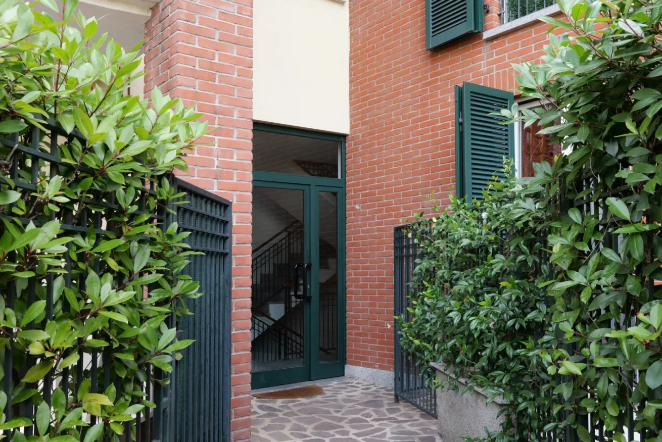 Entrada de un edificio de ladrillo con una puerta verde oscura y plantas frondosas.