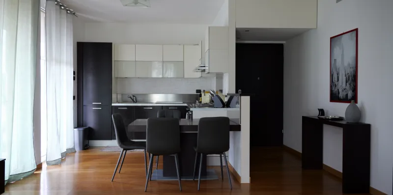 A bright kitchen and dining area with dark seating beside tall windows.