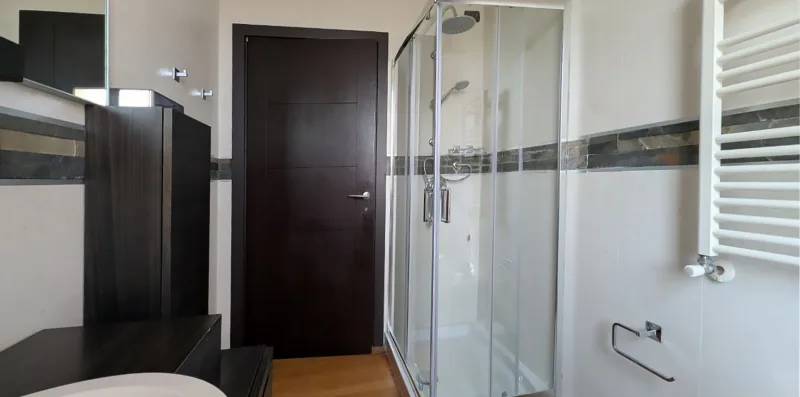 Un baño con una ducha de cristal y muebles de madera oscura.