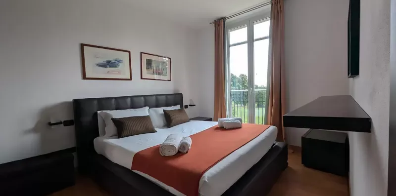 Un dormitorio con una cama vestida con ropa blanca y una manta naranja.