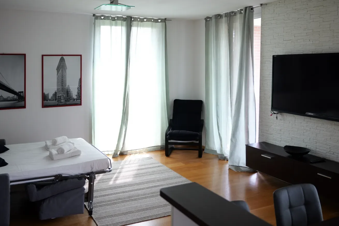 Un dormitorio luminoso con una cama, un sillón y un televisor.