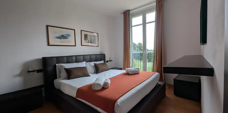 A bedroom with a bed dressed in white linens and an orange runner.