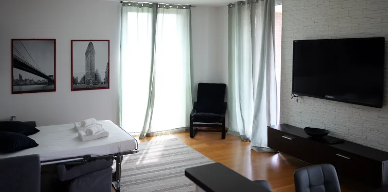 Un dormitorio luminoso con una cama, una silla y un televisor en la pared.