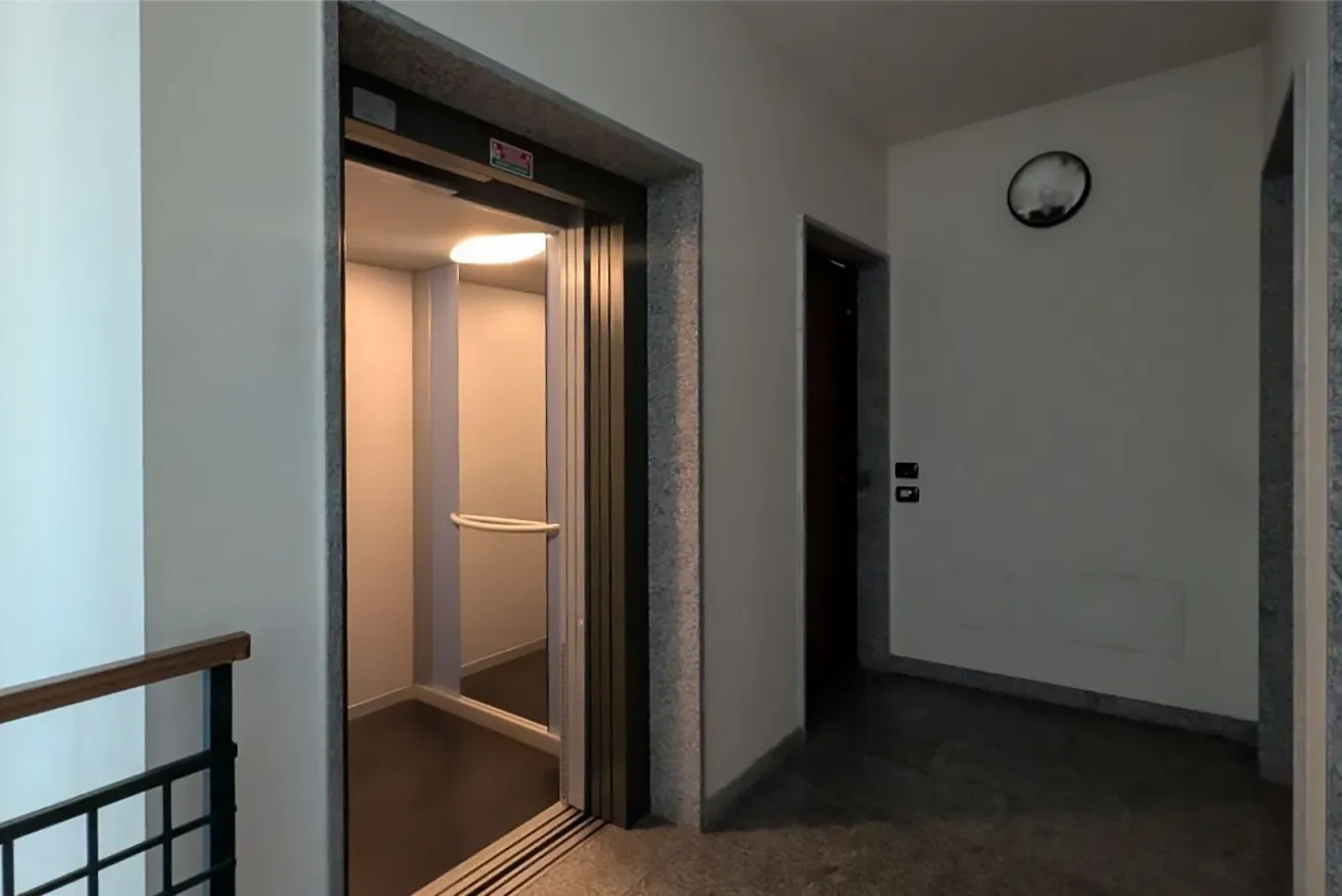 Un ascensor se abre a un pasillo interior con piso oscuro.