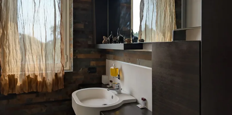 Un lavabo de baño con espejo junto a una ventana con cortinas.