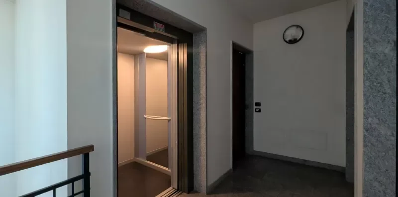 Un pasillo interior con un ascensor abierto y una puerta oscura.