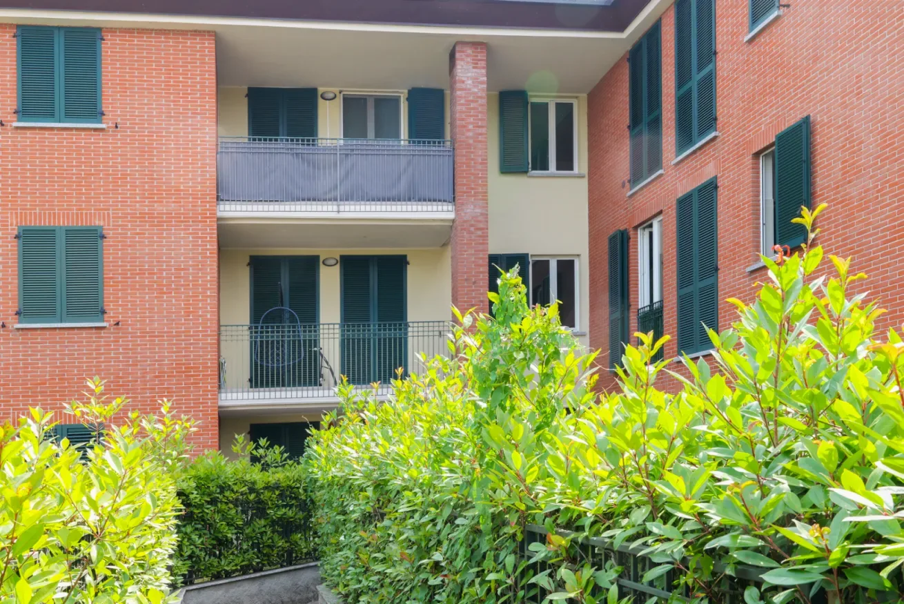 Un edificio de apartamentos con balcones y arbustos frondosos al frente.