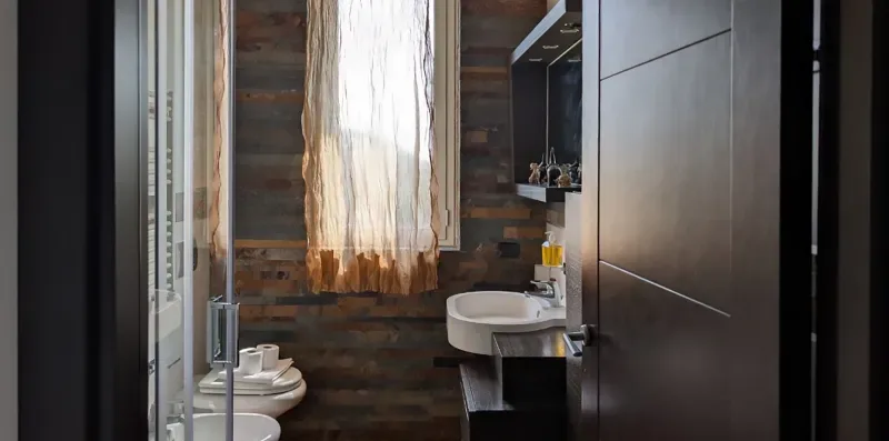 Un baño con lavabo e inodoro junto a una ventana con cortinas translúcidas.