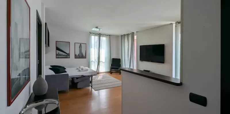Una sala de estar con asientos, un televisor y ventanas luminosas.