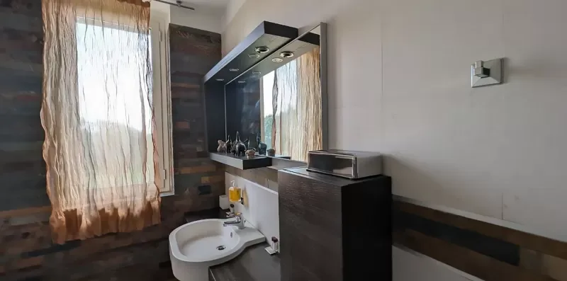 Un tocador de baño con lavabo y espejo está junto a una ventana con cortinas.