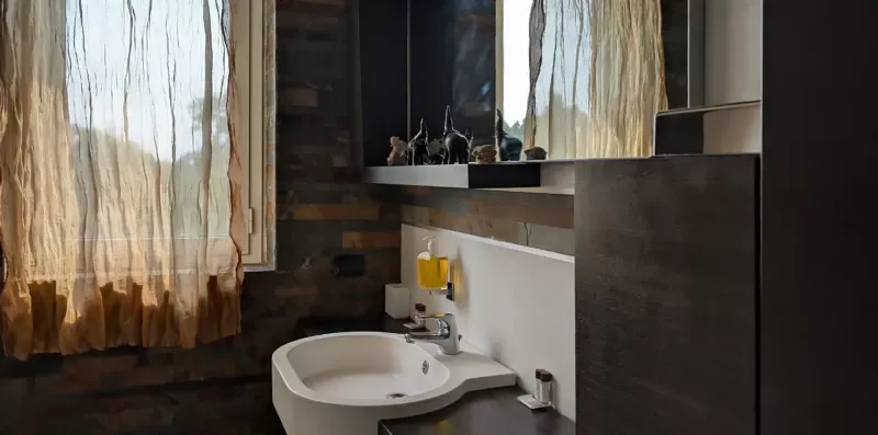 Un tocador de baño con lavabo está debajo de un espejo, junto a una ventana con cortinas.