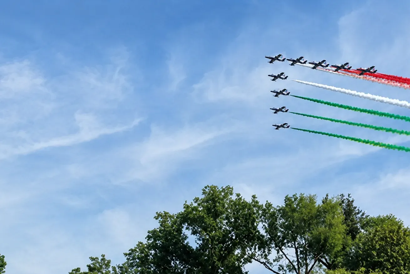 Aeronaves vuelan en formación sobre las copas de los árboles, dejando estelas de humo de colores en el cielo.