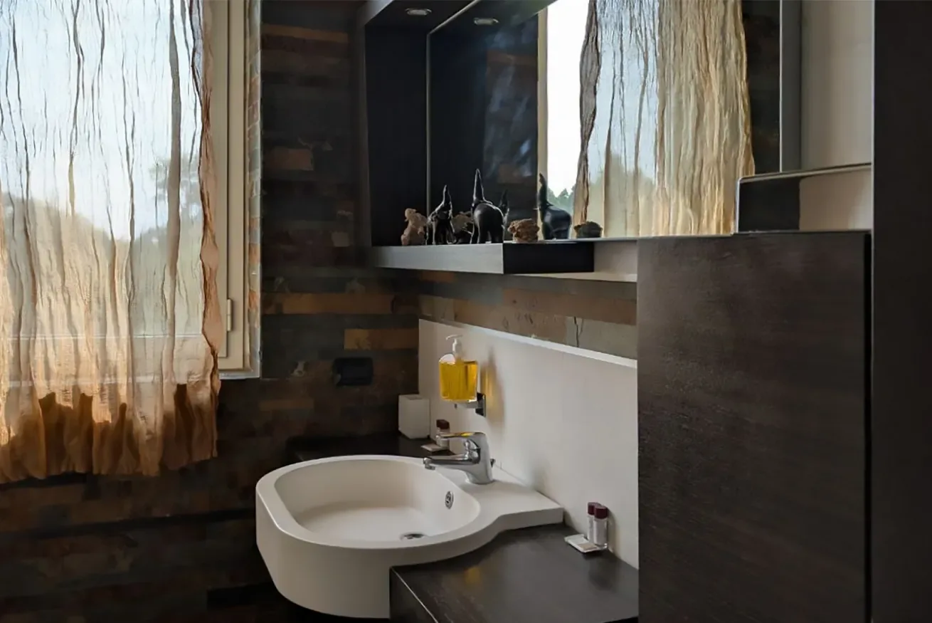 Un lavabo de baño con una pila blanca y una ventana con cortina.