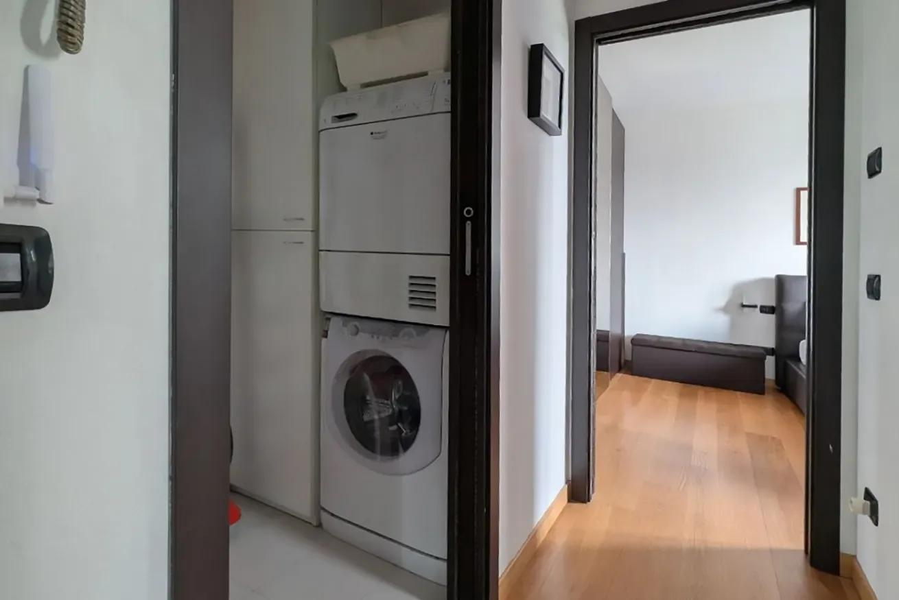 Una zona de lavandería con lavadora y secadora apiladas da a un pasillo.
