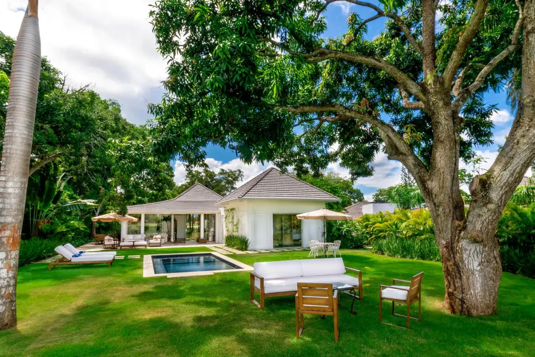 A landscaped garden with a swimming pool, outdoor seating, and a low white building.