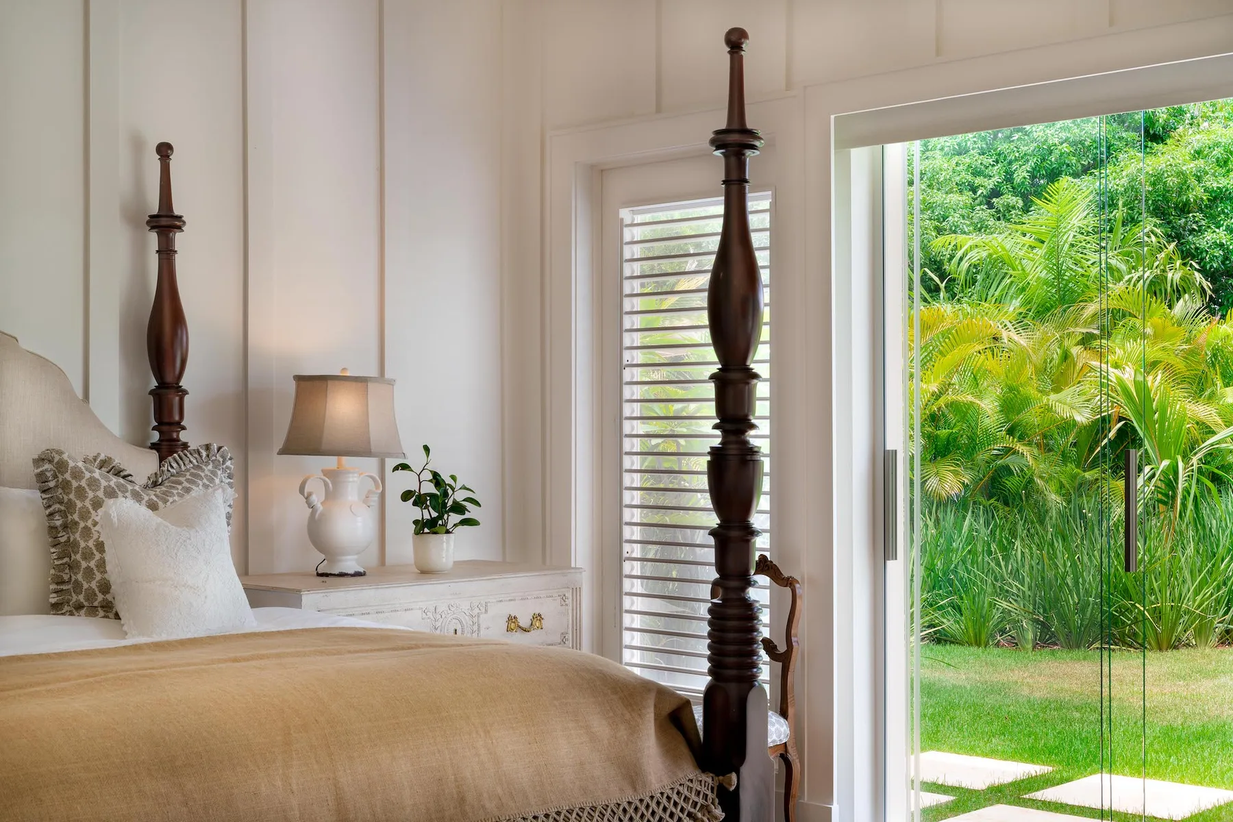 A bedroom with a neatly made bed and a large window overlooking greenery.