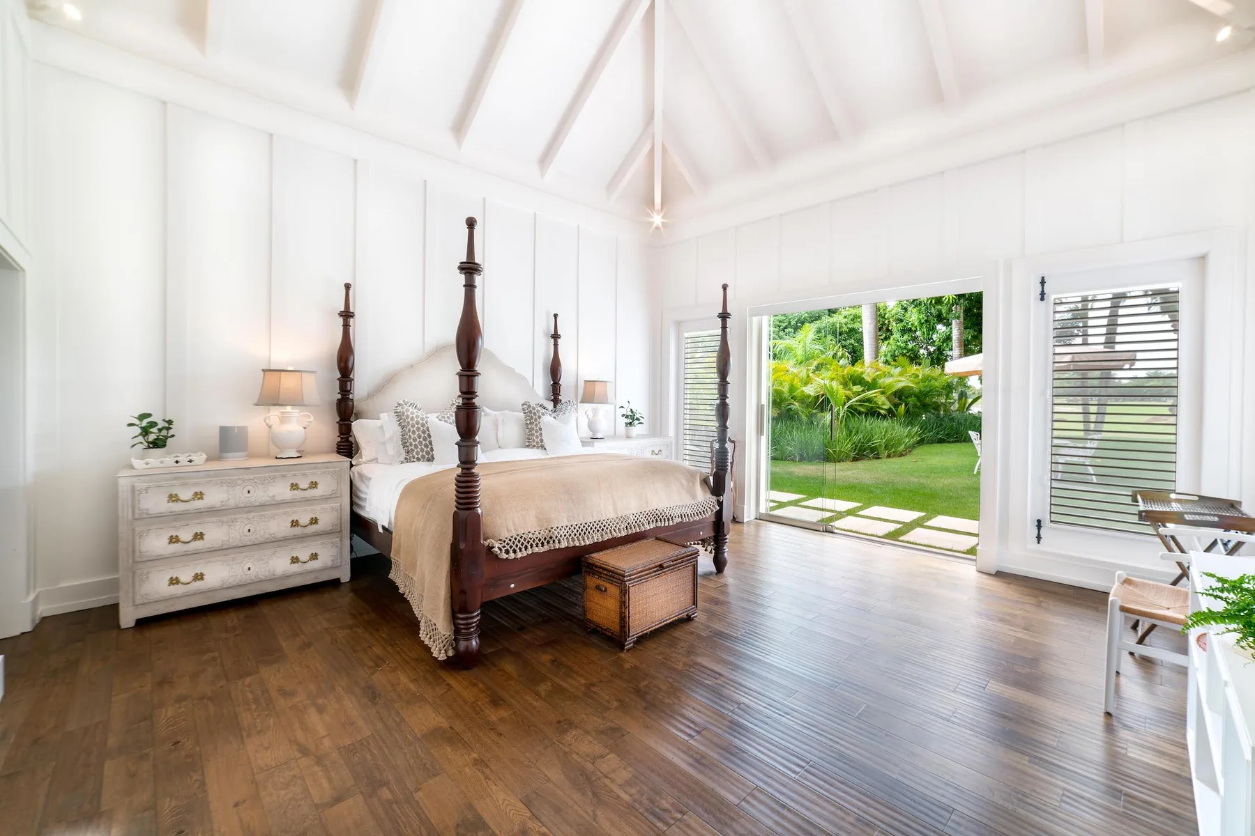A bright bedroom with a four-poster bed and glass doors opening onto a garden.