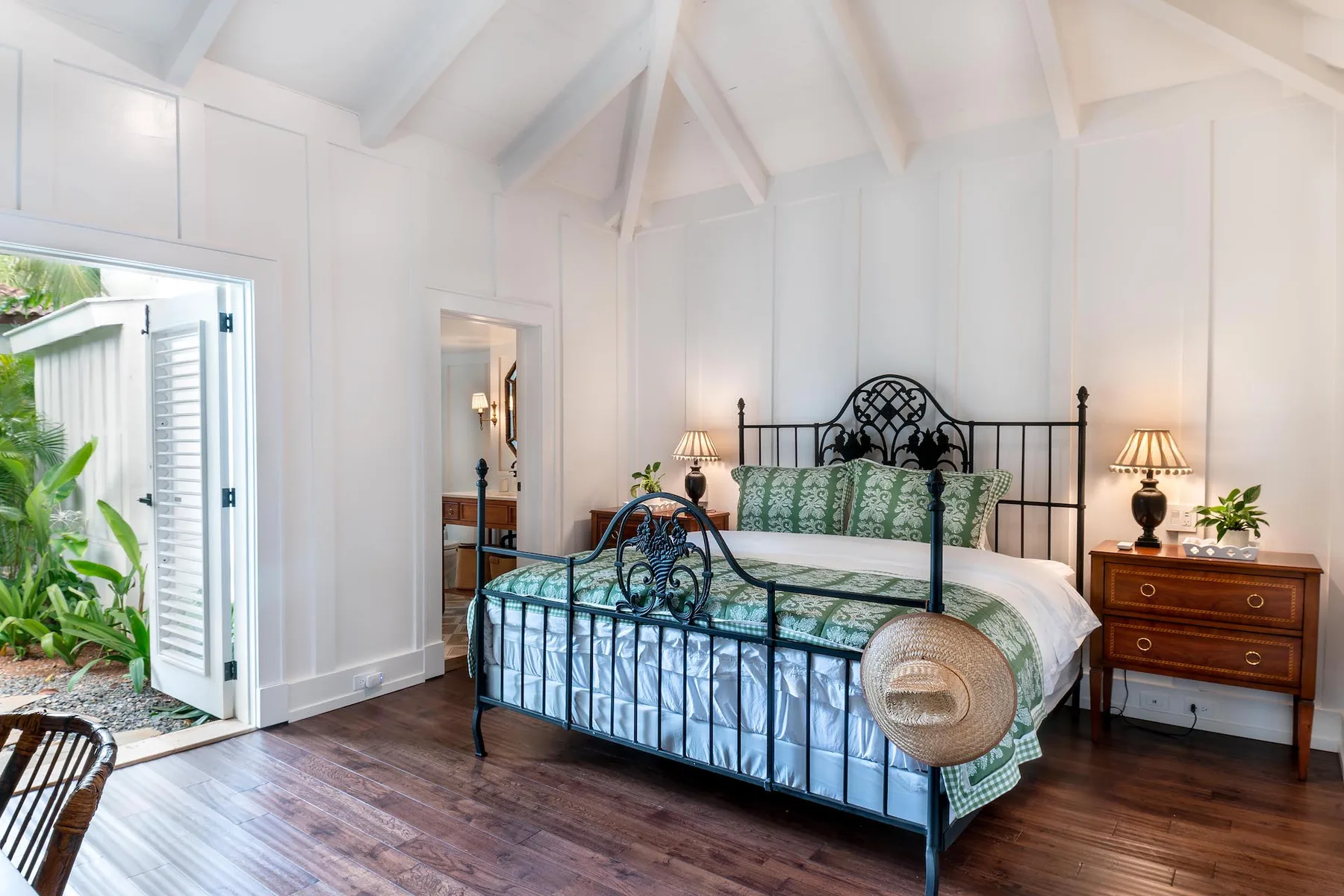 A bright bedroom with a metal bed, green bedding, and wooden bedside tables.